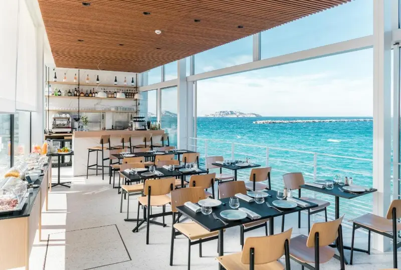 Une salle lumineuse avec des tables dressées face à la mer.
