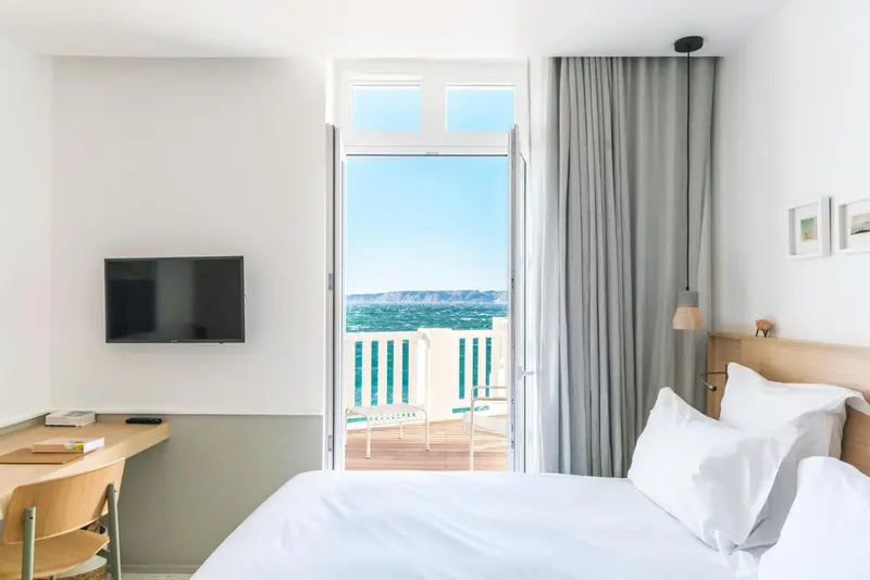 Une chambre lumineuse avec un lit blanc et un balcon donnant sur la mer.