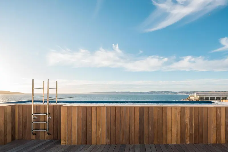 Une piscine à débordement avec une vue sur la mer et le ciel nuageux.