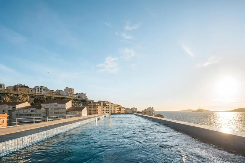 Une piscine à débordement surplombe la mer sous un ciel bleu.