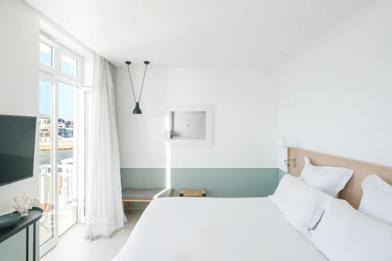 Une chambre lumineuse avec un lit blanc et une vue sur la mer.