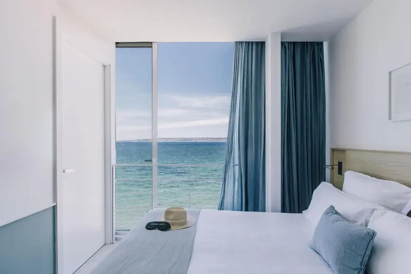 Une chambre lumineuse avec un lit face à une grande baie vitrée donnant sur la mer.