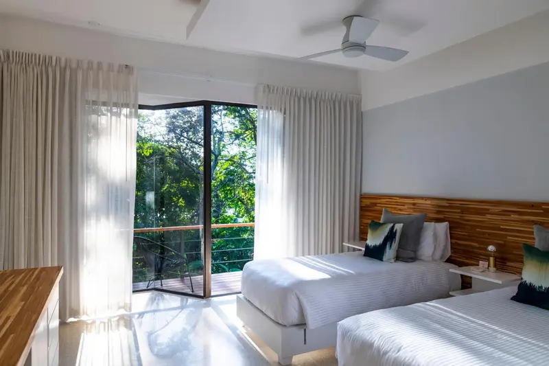 Chambre lumineuse avec deux lits simples et vue sur la végétation.