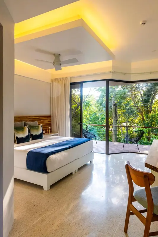 Une chambre lumineuse avec un grand lit et un accès à une terrasse verdoyante.