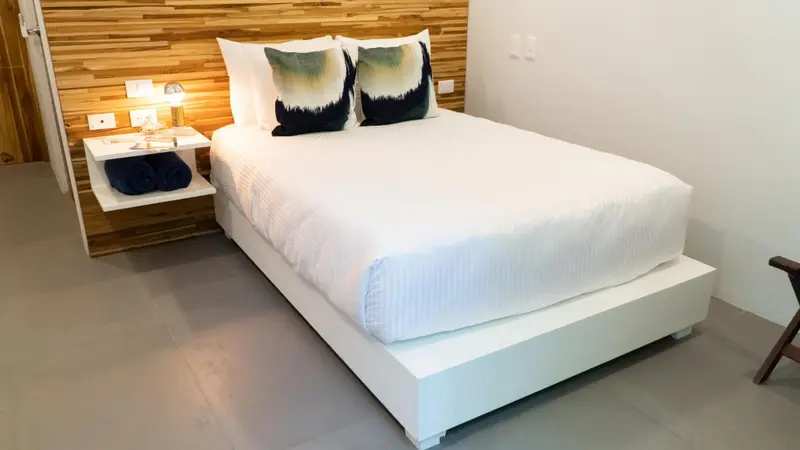 Une chambre lumineuse avec un lit recouvert de draps blancs et des oreillers colorés.