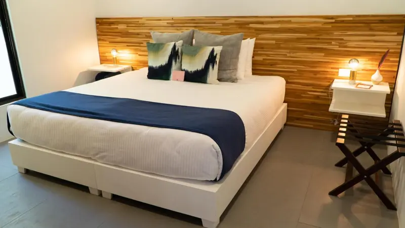 Une chambre lumineuse avec un grand lit recouvert d'une courtepointe bleue et de plusieurs oreillers.