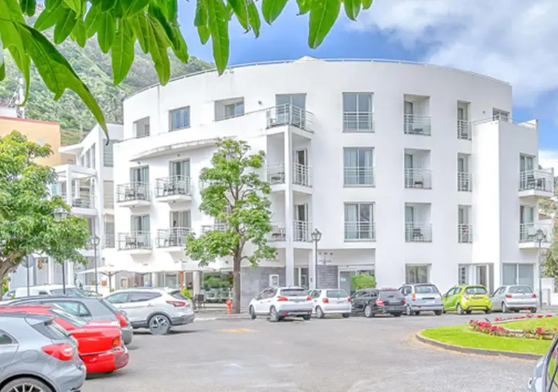 Bâtiment blanc moderne avec des balcons et un parking devant.