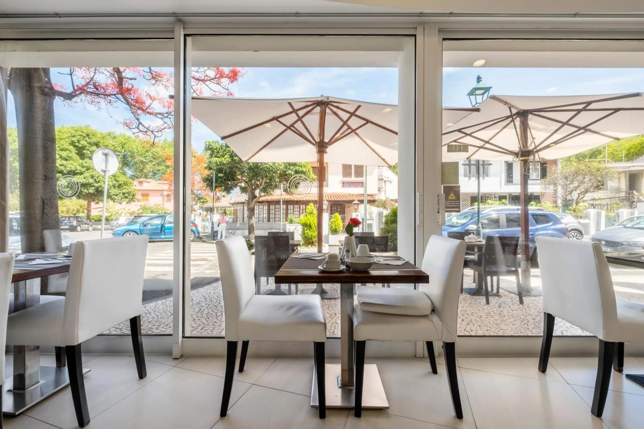 Tables et chaises blanches disposées devant de grandes baies vitrées donnant sur une terrasse ombragée.