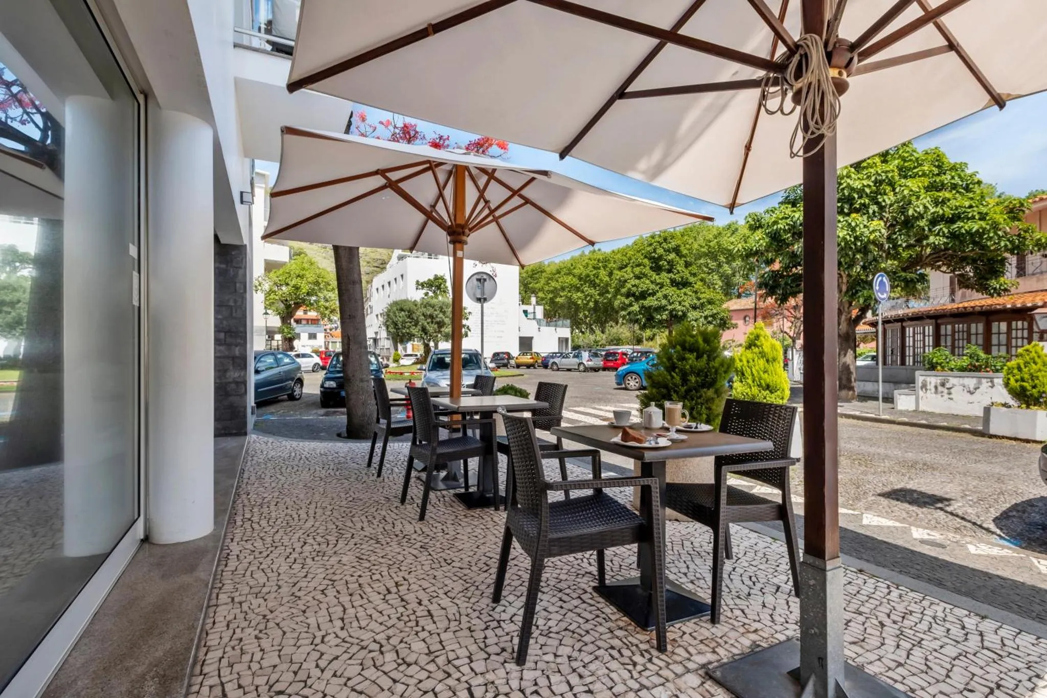 Tables et chaises disposées sur une terrasse ombragée près d'une route.