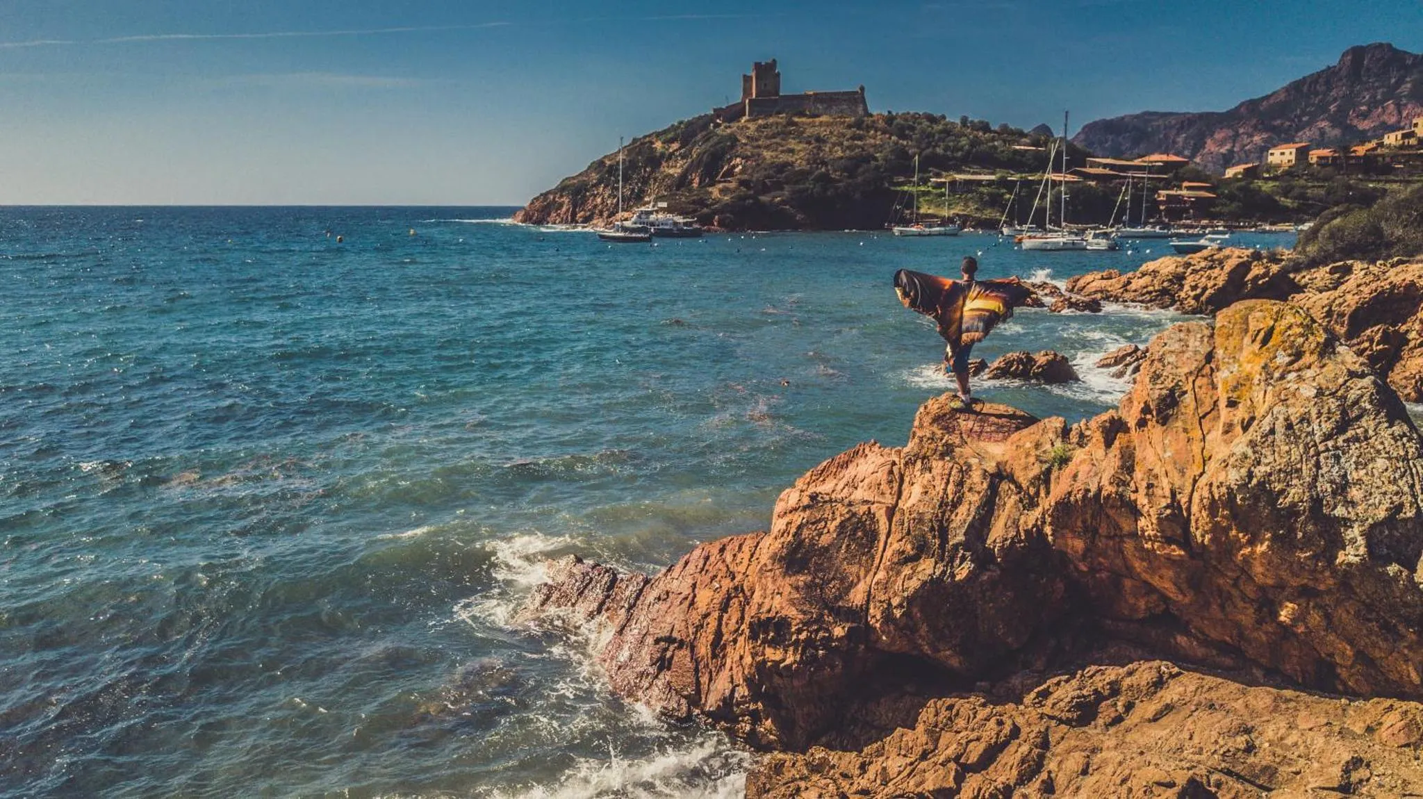 Une personne se tient au bord d'une falaise rocheuse surplombant la mer.