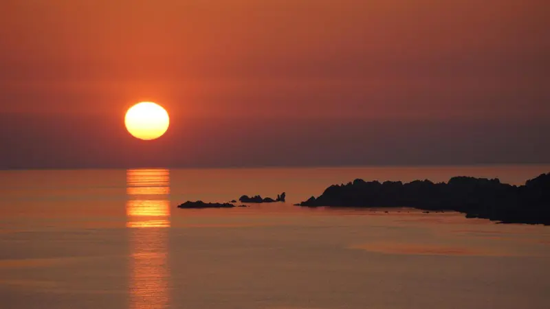 Le soleil se couche sur la mer, illuminant l'horizon d'une lumière orangée.
