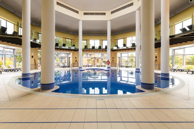 Une piscine intérieure lumineuse avec des colonnes et des transats.