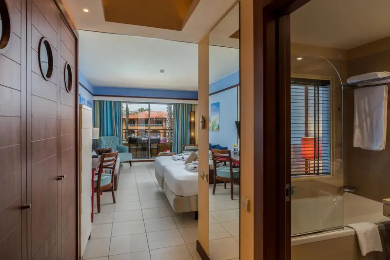 Une chambre lumineuse avec un lit double et un coin salon donnant sur une terrasse.