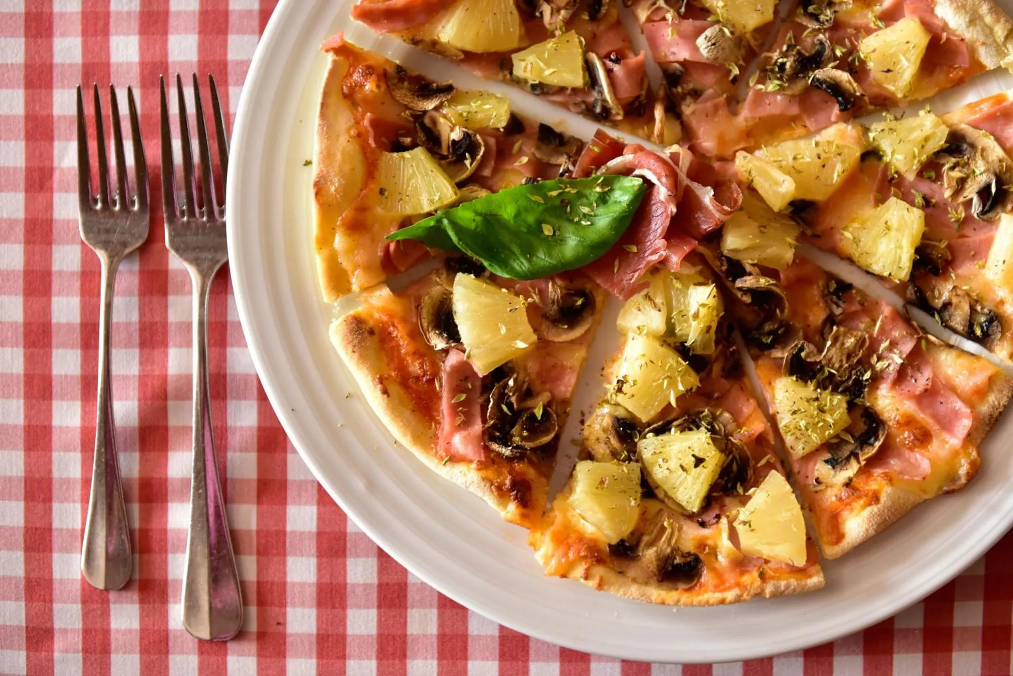 Une pizza garnie de champignons, de jambon et d'ananas est présentée sur une assiette.