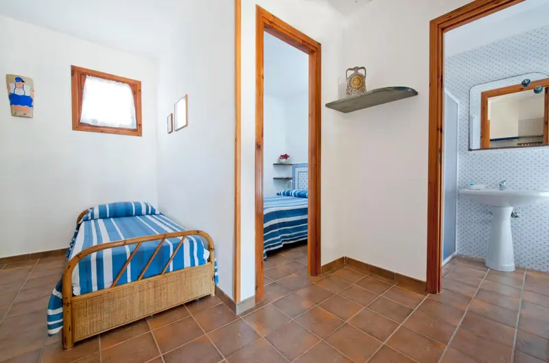 Une banquette en osier rayée se trouve dans un couloir menant à une chambre et une salle de bain.
