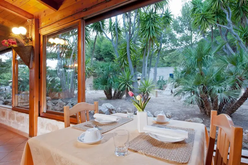 Une table est dressée devant une grande baie vitrée donnant sur une végétation luxuriante.