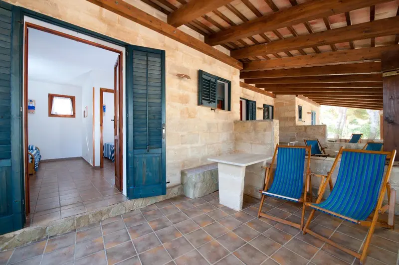 Terrasse ombragée avec mobilier de jardin et vue sur des chambres.