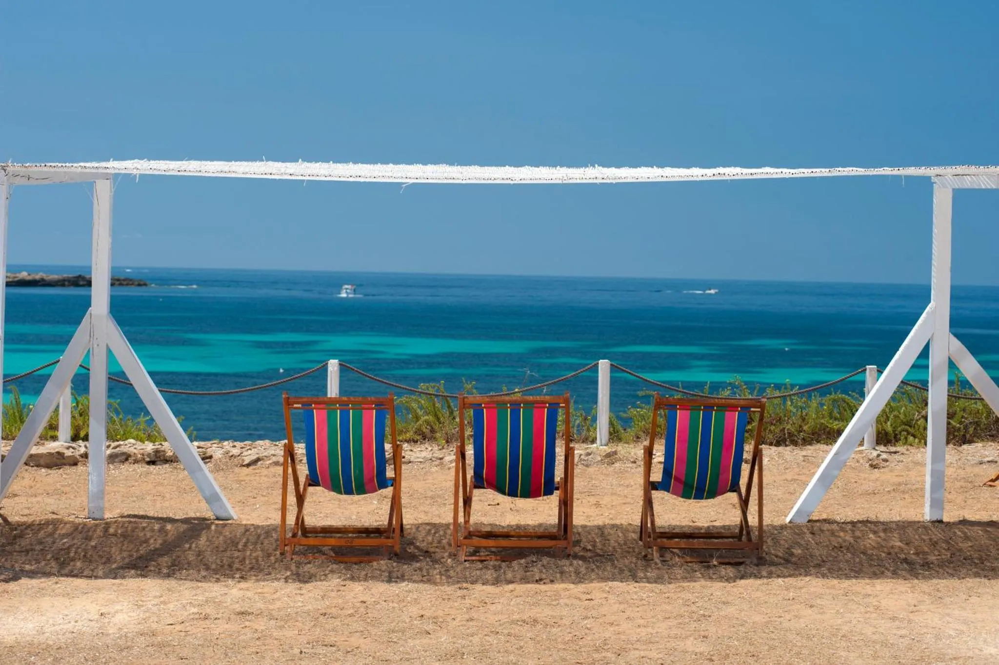 Trois chaises longues colorées sont alignées face à la mer turquoise.