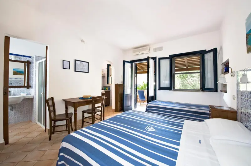 Une chambre lumineuse avec un lit recouvert d'une couverture rayée et une petite table à manger près de la fenêtre.