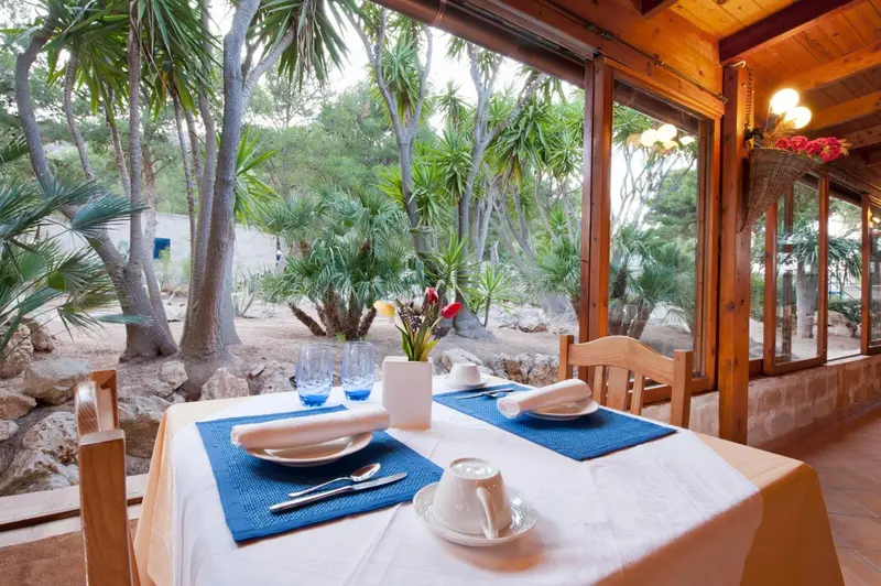 Une table est dressée pour un repas dans une salle lumineuse donnant sur un jardin.