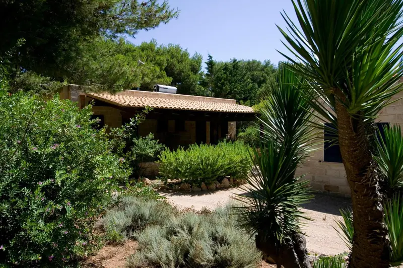 Bâtiment en pierre avec toiture en tuiles, entouré de végétation luxuriante et d'un jardin soigné.