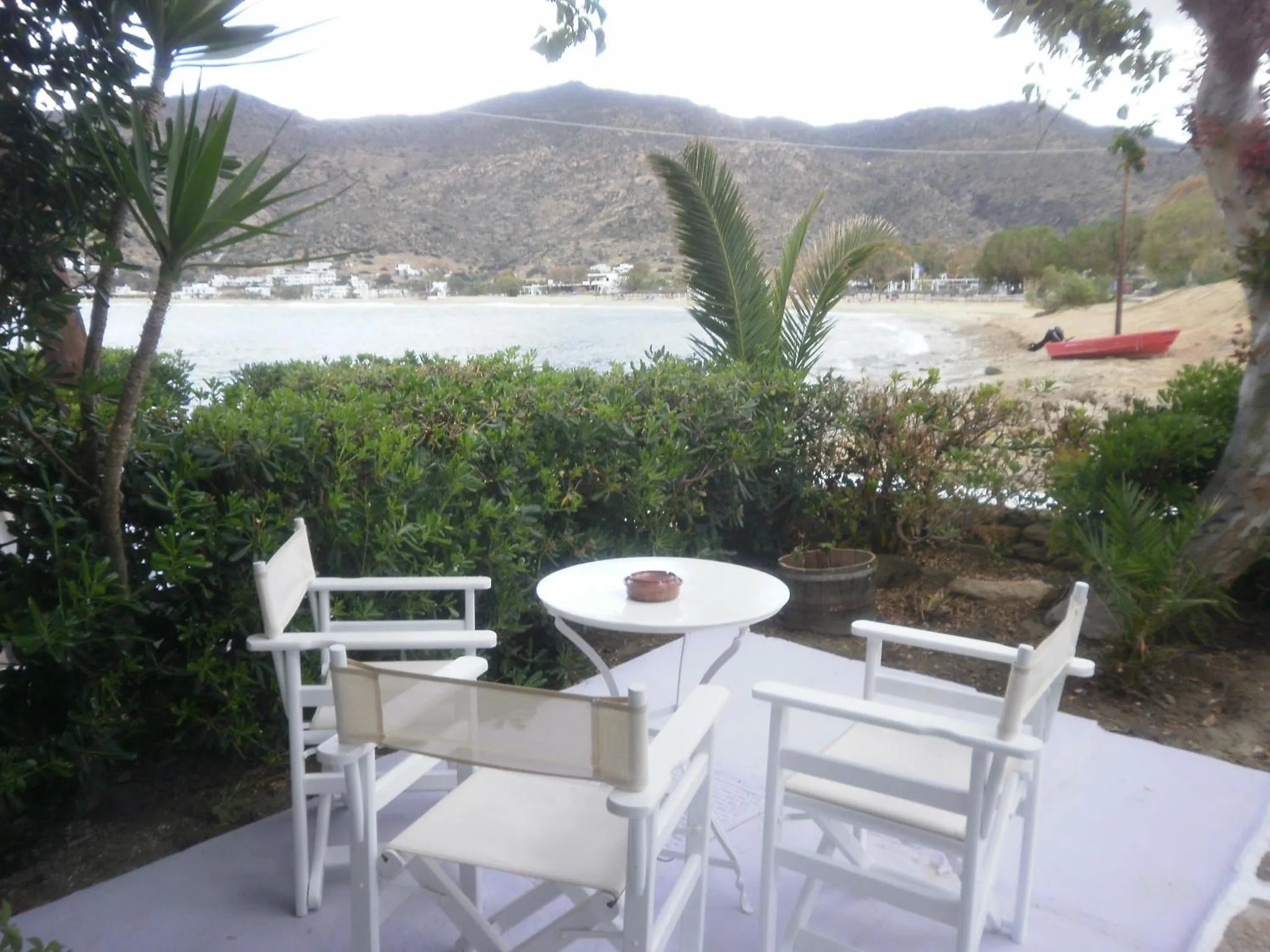 Une table ronde et des chaises blanches sont disposées sur une terrasse ensoleillée avec vue sur la mer.