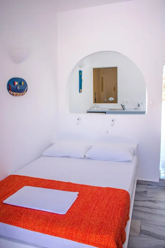 Une chambre lumineuse avec un lit recouvert d'une couverture orange et un miroir en arc de cercle.
