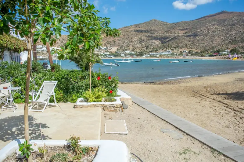 Terrasse ensoleillée avec mobilier de jardin donnant sur une plage de sable et la mer.