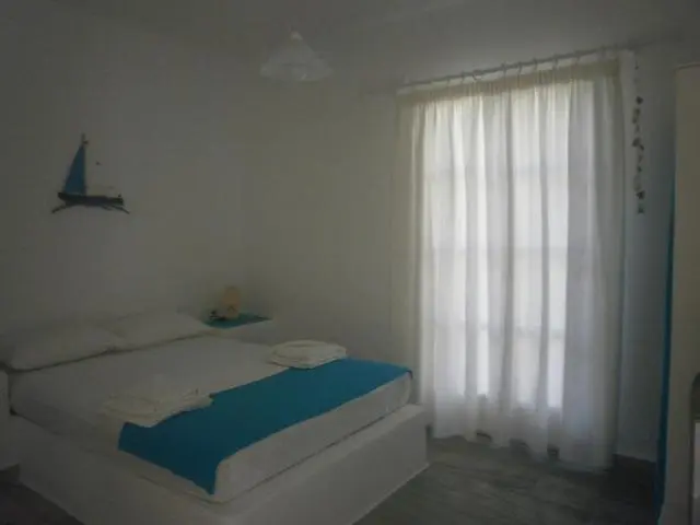 Une chambre lumineuse avec un lit recouvert d'une couverture bleue et une fenêtre voilée.