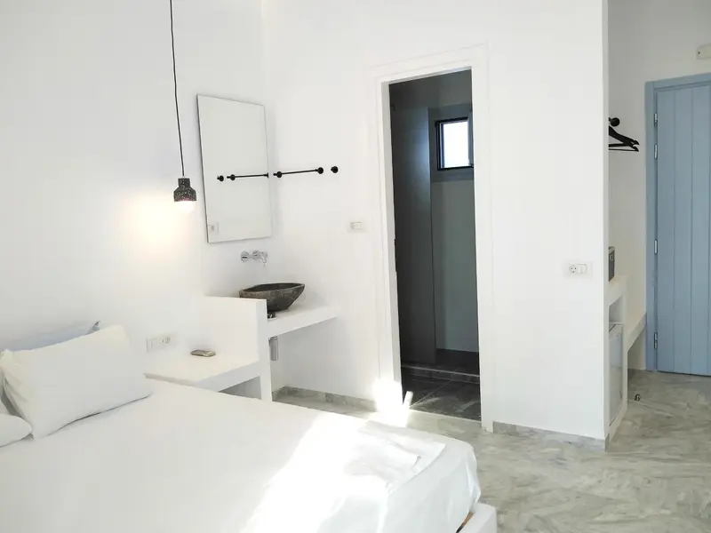 Une chambre lumineuse avec un lit blanc et un accès à une salle de bain.