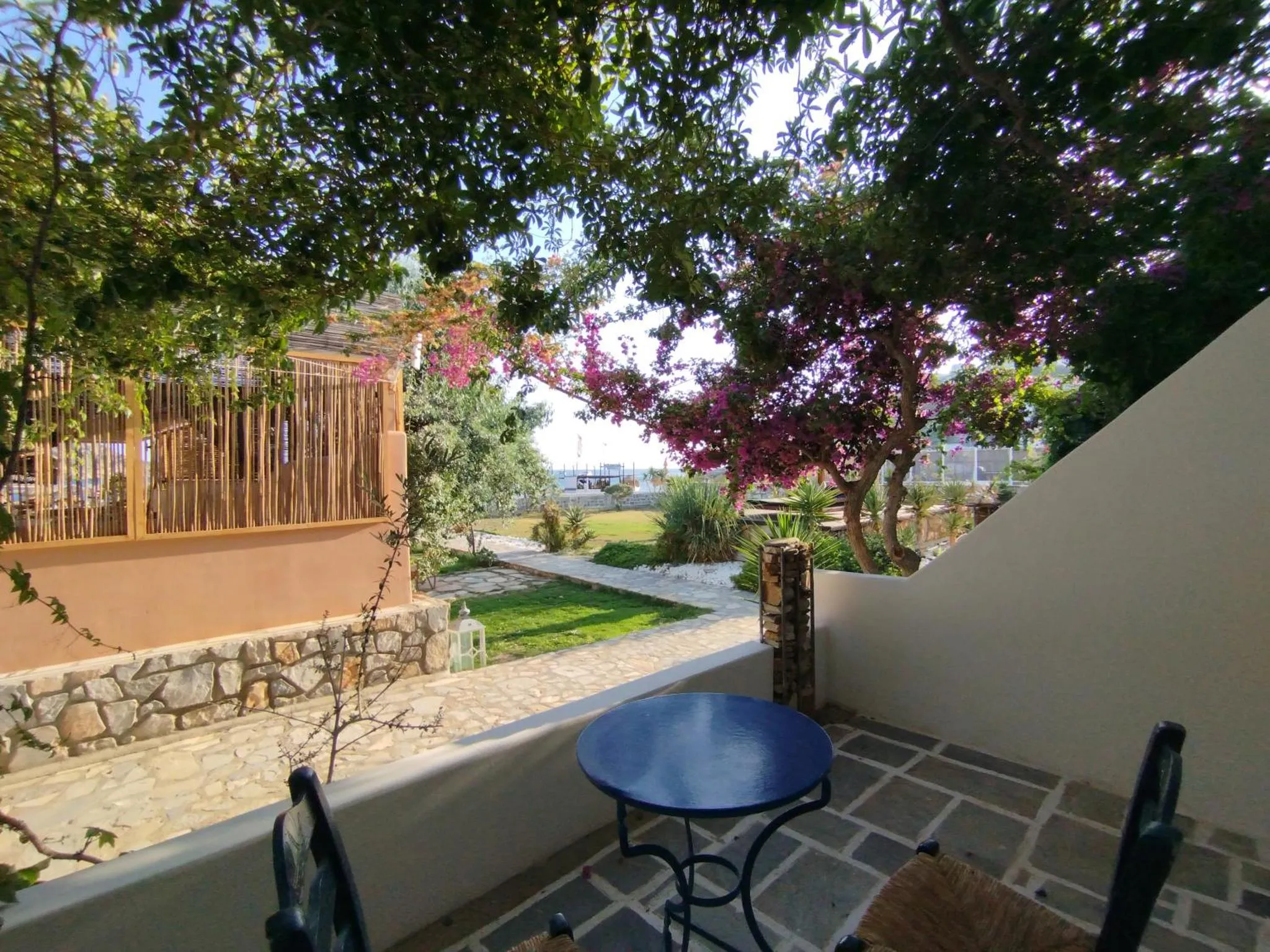 Une terrasse ombragée donne sur un jardin verdoyant et une vue sur la mer.