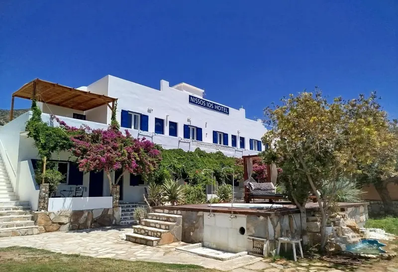 Bâtiment blanc à deux étages avec des volets bleus et une végétation luxuriante devant.