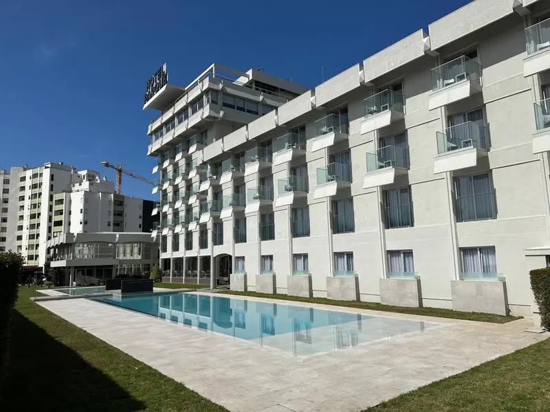 Bâtiment moderne blanc avec des balcons et une piscine rectangulaire au premier plan.