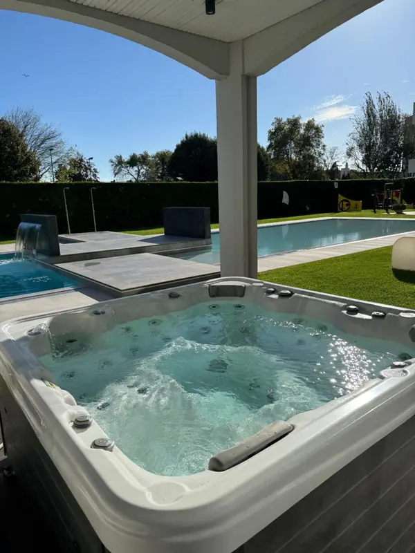 Un jacuzzi extérieur avec une piscine au loin sous un ciel bleu.