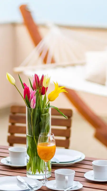 Une table en bois est décorée de fleurs colorées, de vaisselle et de boissons.