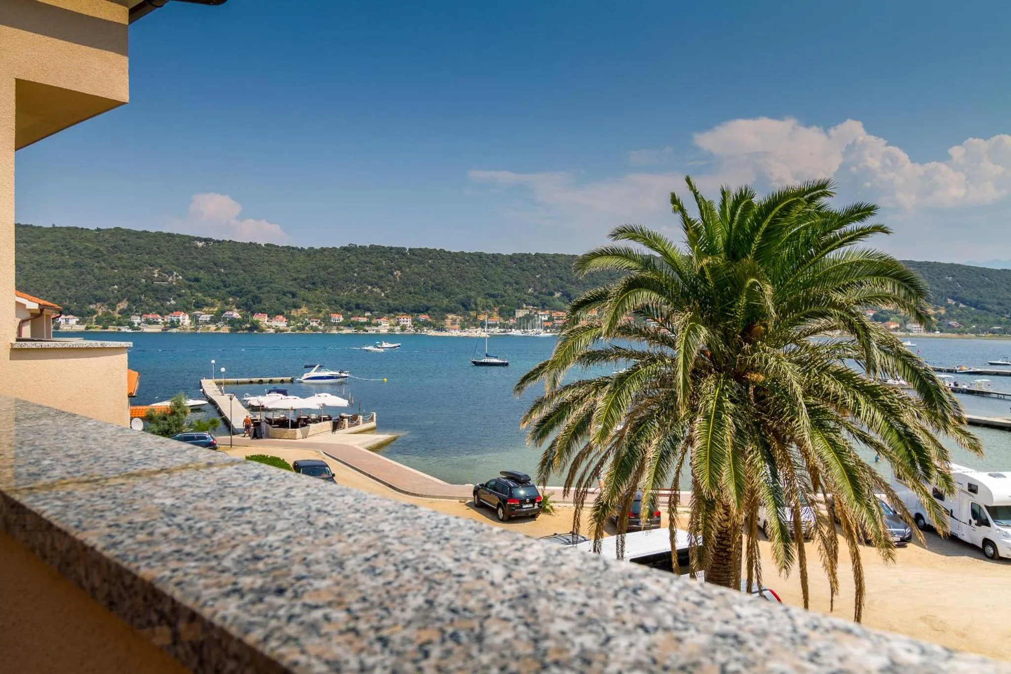 Vue sur la mer depuis un balcon avec un palmier au premier plan.
