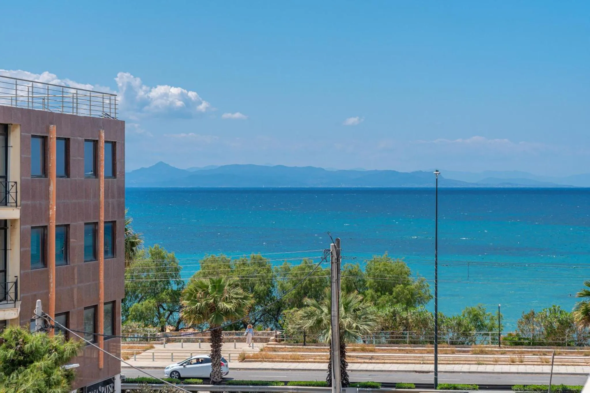 Vue sur la mer depuis un bâtiment avec des palmiers au premier plan.