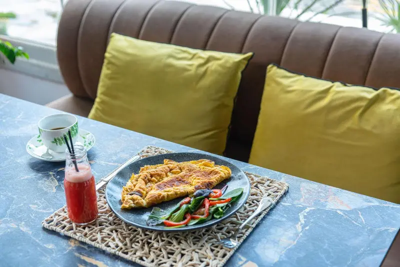 Une table est dressée avec un petit-déjeuner composé d'une omelette, d'une boisson et d'une tasse de thé.