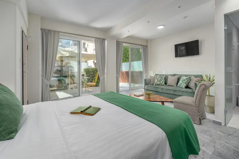 Une chambre lumineuse avec un grand lit et un coin salon donnant sur une terrasse.