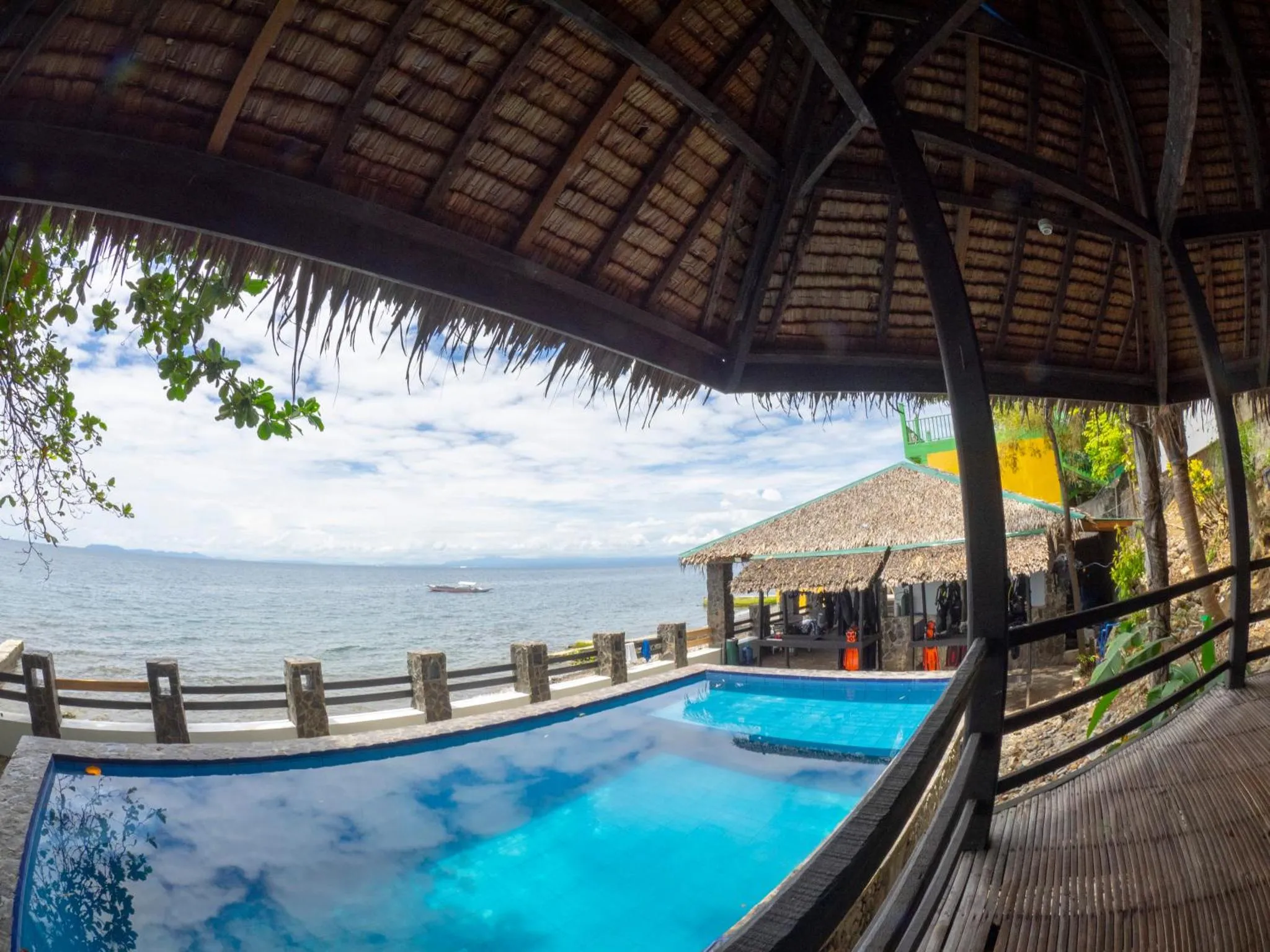 Une piscine turquoise bordée d'une terrasse en bois offre une vue sur la mer et le ciel nuageux.