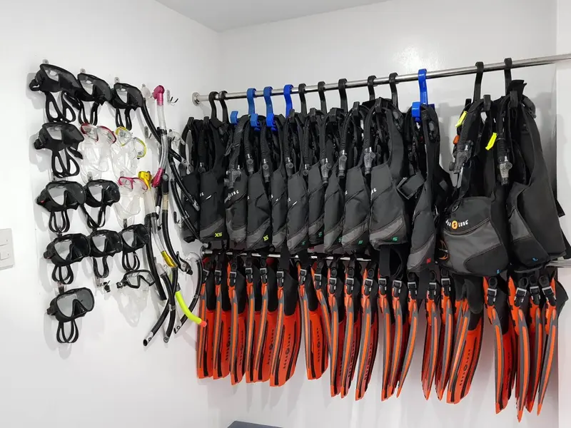 Rangée de masques, tubas et gilets stabilisateurs accrochés au mur.