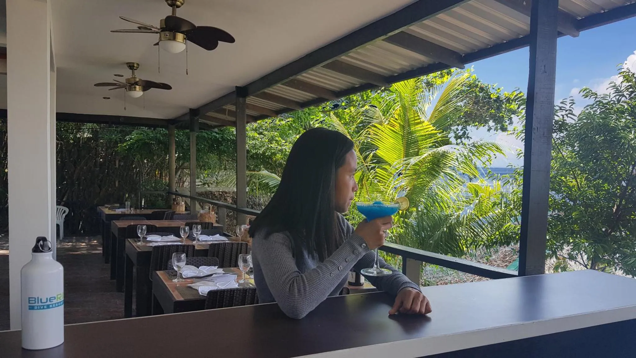 Une personne assise à une table en terrasse, face à la mer.