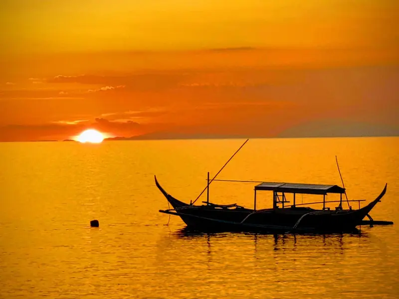 Un bateau de pêche traditionnel repose sur une mer calme au coucher du soleil.