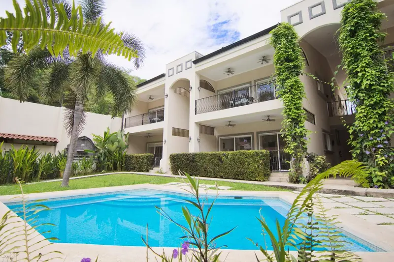 Façade d'un bâtiment blanc orné de végétation avec une piscine au premier plan.