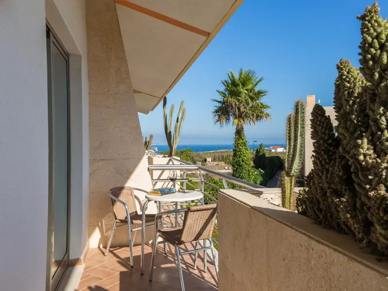 Terrasse avec mobilier d'extérieur et vue sur la végétation et la mer.