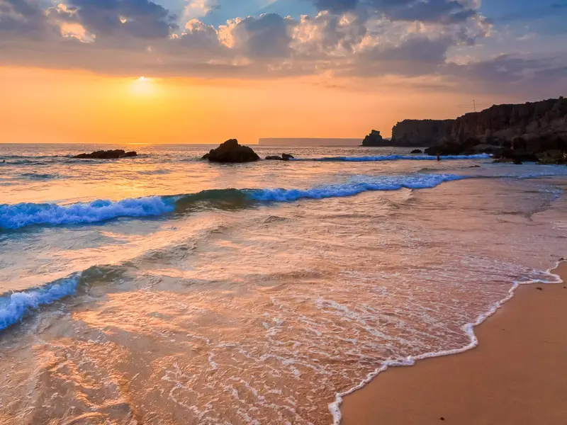 Une plage de sable doré baignée par les vagues au coucher du soleil.