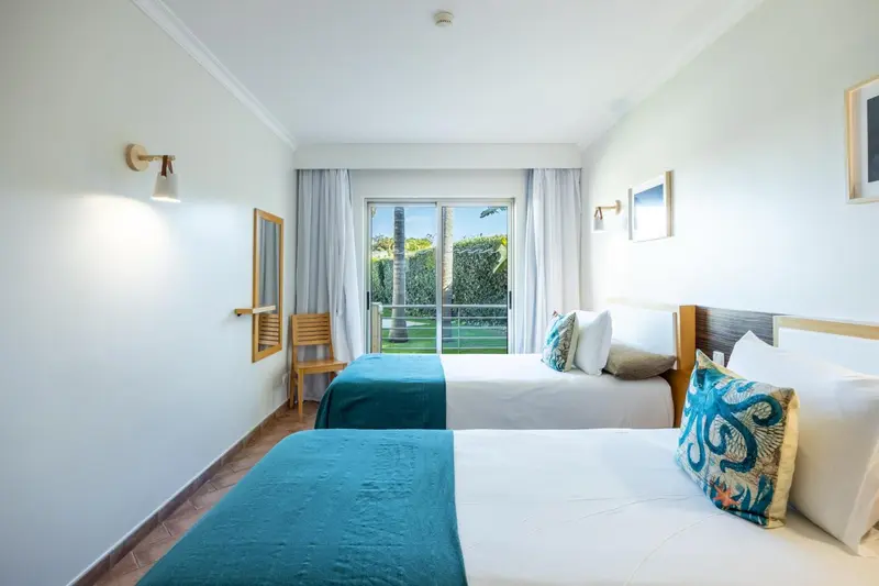 Chambre lumineuse avec deux lits simples et vue sur un jardin.