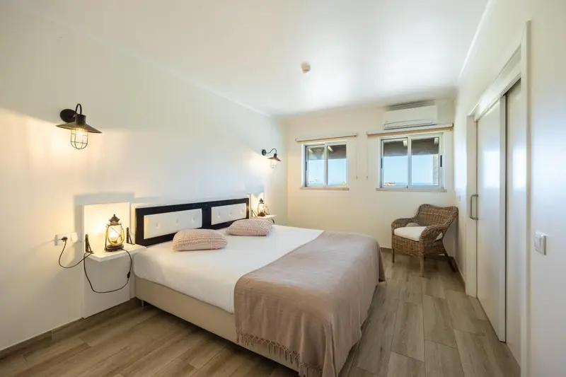 Une chambre lumineuse avec un grand lit et un fauteuil en osier.