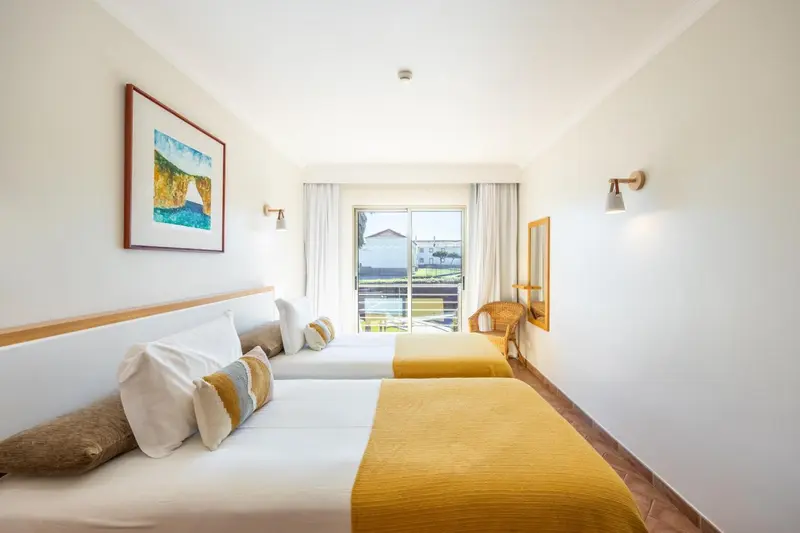 Chambre lumineuse avec deux lits simples et une vue sur l'extérieur.
