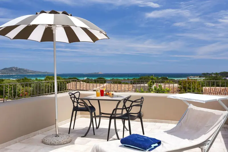 Une table et des chaises sont disposées sur une terrasse ensoleillée avec vue sur la mer.
